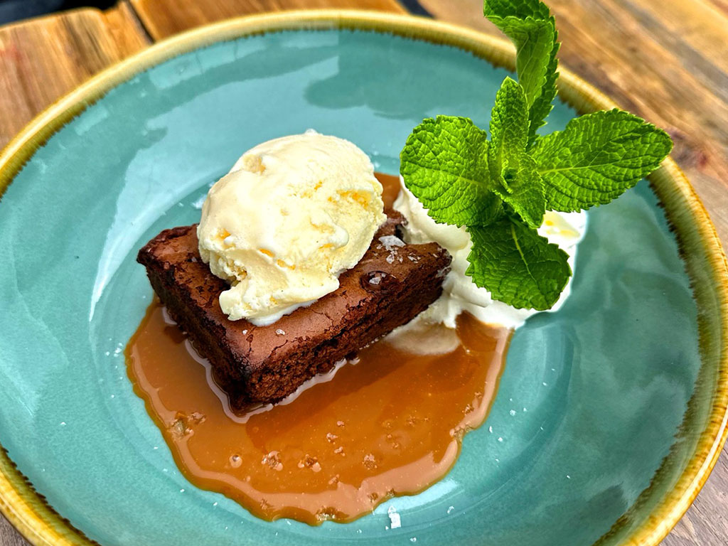 Bilde av brownie på tallerken, smeltet karamellsaus og is
